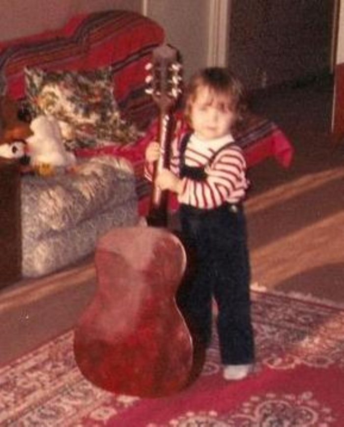 Photo d'archive de Sylvain Peter à l'âge de 2 ans, posant à côté d'une guitare classique aussi grande que lui.